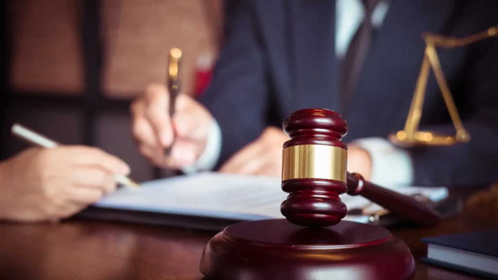 Close-up of a gavel and legal documents with a person signing in the background