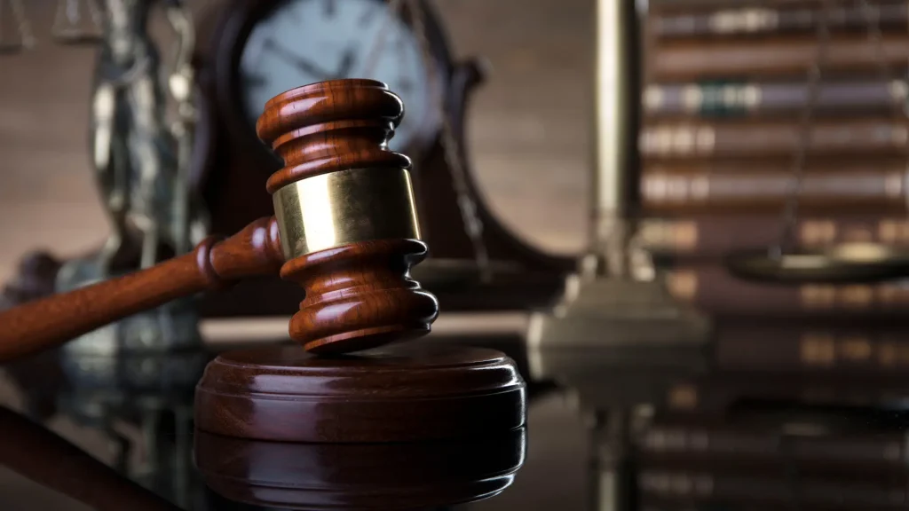 Close-up of a gavel with a clock and law books in the background.